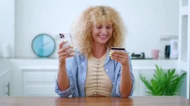 Çekici beyaz saçlı kadın internette ödeme yapıyor, kredi kartı tutuyor ve internet üzerinden akıllı telefon alışverişi yapıyor.