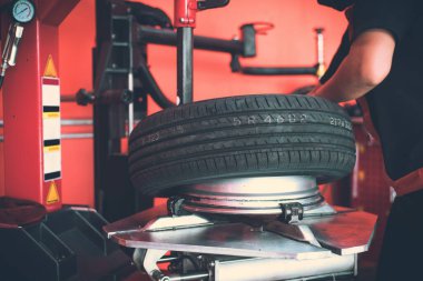 Modern araba tamircinin tekerleklerini ve lastiklerini değiştirmesini bekliyor. Tamirci arabanın lastiklerini değiştiriyor.