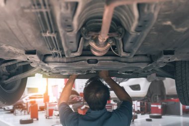 asian Car Mechanic Adjusting Tension in Vehicle Suspension Element. Professional Automotive Service.