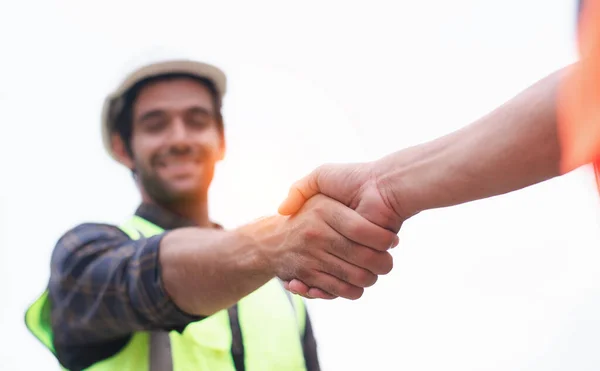 Koruyucu miğferler ve yelekli yakışıklı inşaat mühendisi ofis merkezinde çalışırken el sıkışıyor