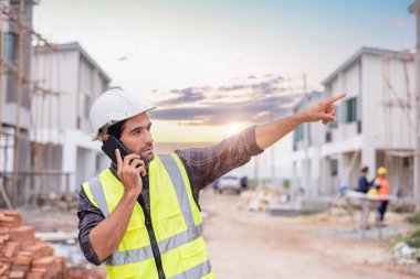 Güvenlik kaskı ve yelek giyen mühendis adam dışarıdaki proje bakımını her gün kontrol ediyor. İnşaat sahasında kasketi olan inşaat mühendisi veya mimar.