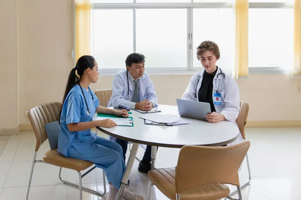 Multiracial medical team having a meeting with doctors in white lab coats and surgical scrubs seated at a table discussing a patients records, Medical team checking Xray results.