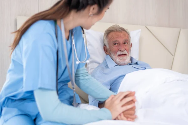 asian female home nursing holding hand of older male on the bed and encouraging patient,Senior man in hospital bed holding nurse\'s hand,Health concept.