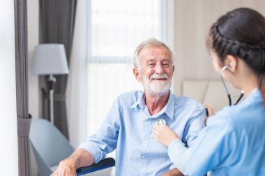 Genç kadın pratisyen hekimi ya da kardiyoloğu steteskop kullanarak kapatın, kalp atışlarını ya da yaşlı yaşlı erkek hastaların sağlık kontrolündeki seslerini dinleyin 