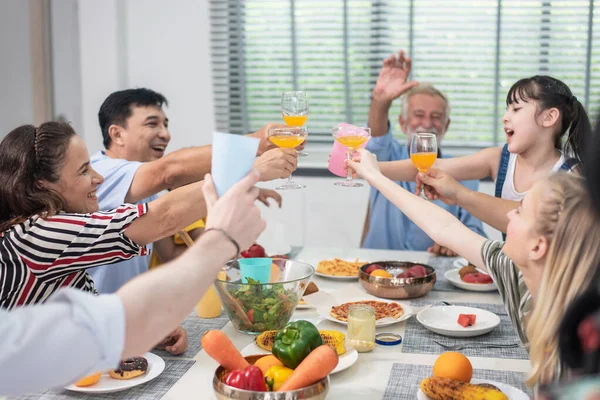 Generations of families have enjoyed gathering around the dining table and having a fun lunch, Happy family having dinner and glasses of orange juice collide in the summer house.