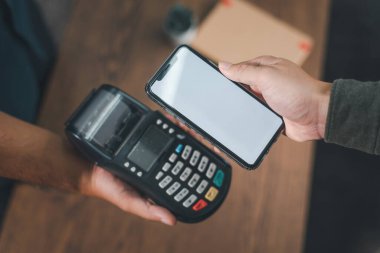 Müşteri faturaları akıllı telefonla NFC teknolojisi kullanarak ödüyor. Özenle seçilmiş bir ödemenin yakın plan çekimi. Faturaları ödemek için elinde cep telefonu tutan bir adam.