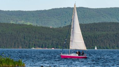 Yelkenli bir tekne gölde yüzüyor.