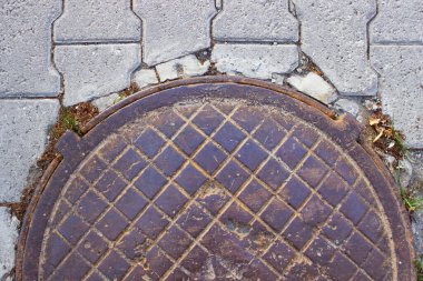 Kentsel kaldırımda yuvarlak tek renkli metal kapak, işaretli kanalizasyon kapağı.