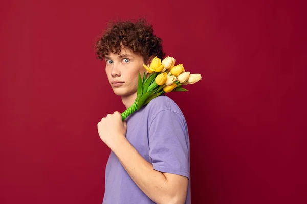 Молодий хлопець тримає жовтий букет квітів фіолетові футболки червоний фон незмінний — стокове фото