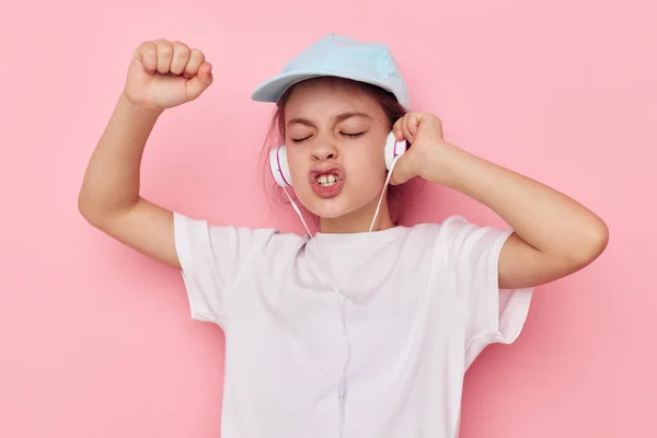 Schattig meisje hoofdtelefoon in een wit t-shirt en een cap roze achtergrond — Stockfoto