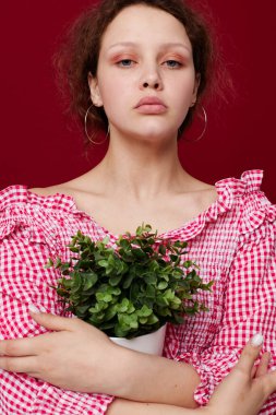 Pembe bluzlu güzel bir kadın beyaz tencerede bir bitkiyle poz veriyor.