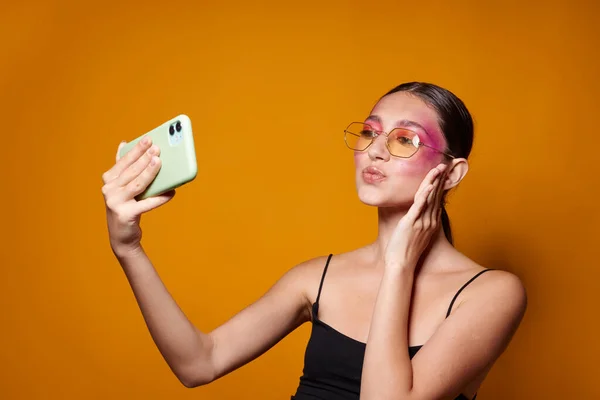 Portrait of beautiful young woman looks at the phone bright makeup posing fashion emotions yellow background unaltered — Foto Stock