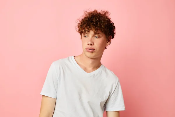 Fiatal göndör hajú férfi pózol ifjúsági stílus fehér póló rózsaszín háttér változatlan — Stock Fotó