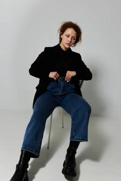 Портрет молодой женщины, сидящей на стуле в черной куртке, позирующей на изолированном фоне без изменений — стоковое фото