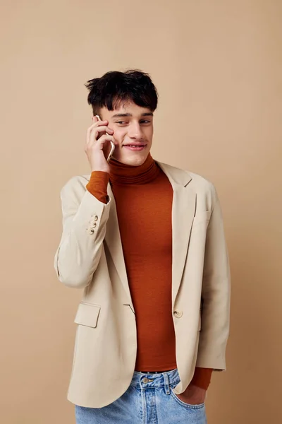Porträtt av en ung man i en beige jacka talar på telefonen ljus bakgrund oförändrad — Stockfoto