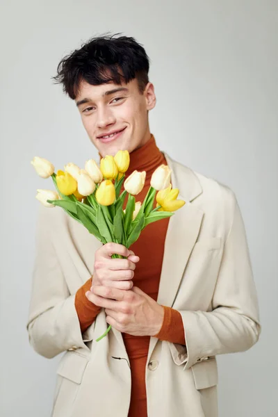 Pretty man in white jacket with a bouquet of yellow flowers elegant style model studio — Stock fotografie