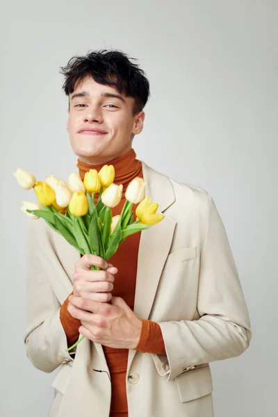 Pretty man in white jacket with a bouquet of yellow flowers elegant style model studio — Stock fotografie