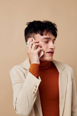 Bej ceketli genç erkek arkadaş telefonla konuşuyor. Hayat tarzını değiştirmemiş.