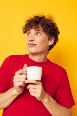 Beyaz kupayla poz veren kıvırcık saçlı genç bir adam ve sarı arka planda değişmemiş bir içeceğin ellerinde.
