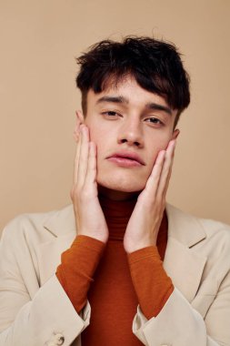 Bej ceketli genç bir adam telefonda konuşuyor. Arkaplanı değiştirilmemiş.