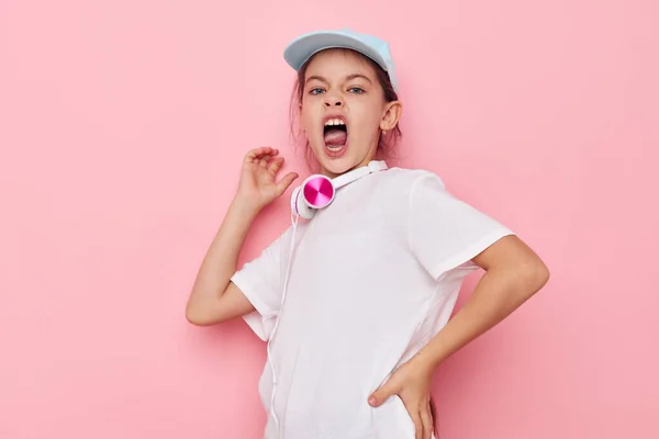 Auriculares de niña bonita en una camiseta blanca y una infancia gorra inalterada — Foto de Stock