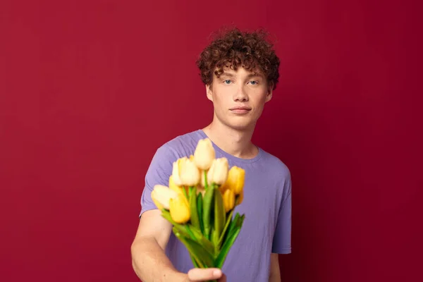 Cute teen holding a yellow bouquet of flowers purple t-shirts red background unaltered — ストック写真