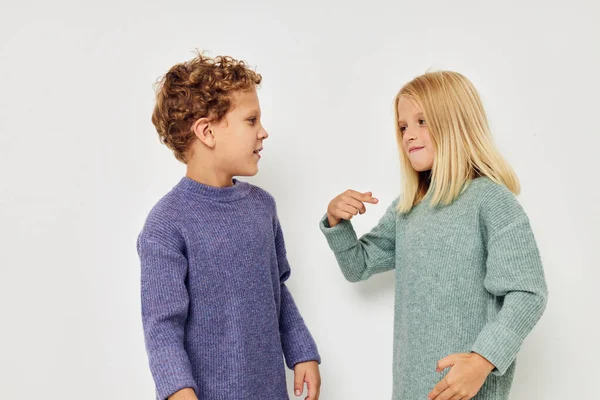 Little boy and girl in multi-colored sweaters posing for fun light background — Foto Stock