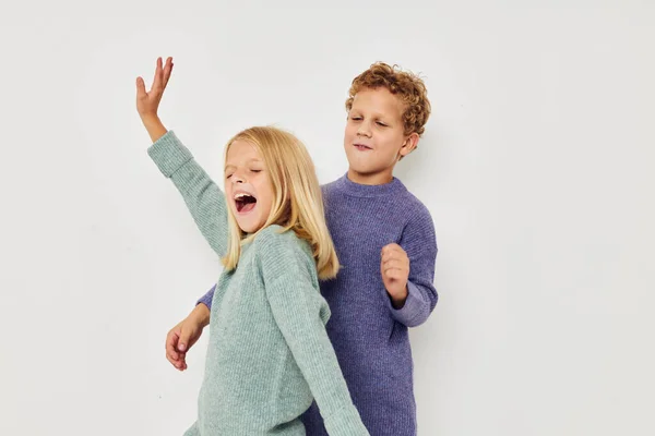 Boy and girl in multi-colored sweaters posing for fun light background — Stock fotografie