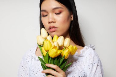 Çiçek buketi olan bir kadın gülüyor. Arka planda hiç değişmemiş bir ışık var.