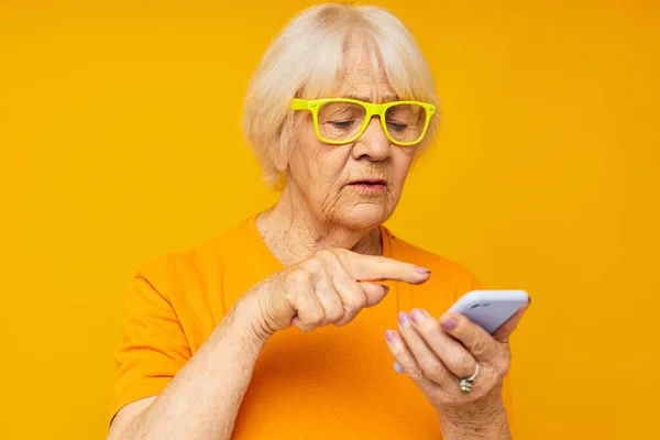 カジュアルなTシャツを着たお年寄り女性が電話で黄色の背景 — ストック写真