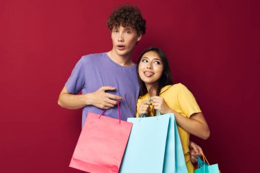 Renkli tişörtlü genç bir çocuk ve kız çantalarla izole edilmiş arka plan alışverişi yapıyorlar.