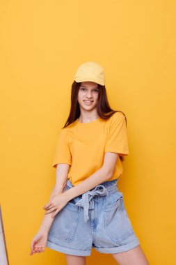 Sarı tişörtlü ve kepli arka planda poz veren güzel bir kadın.