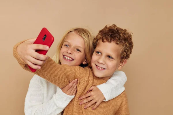 Φωτογραφία δύο παιδιών με πουλόβερ που ποζάρουν για διασκέδαση με το τηλέφωνο απομονωμένο φόντο — Φωτογραφία Αρχείου