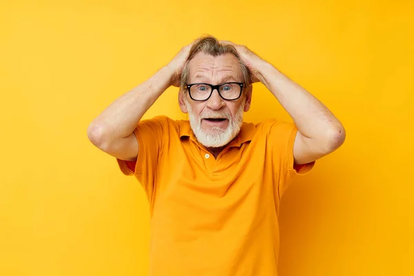 Senior grey-haired man posing yellow tshirt glasses yellow background — Stock fotografie