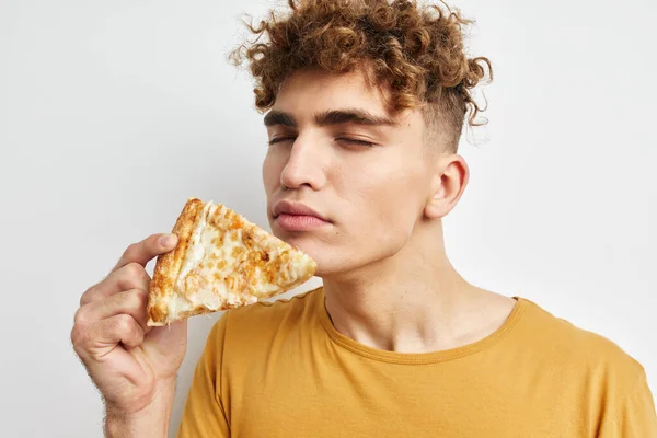 Handsome guy eating pizza posing close-up light background — 图库照片