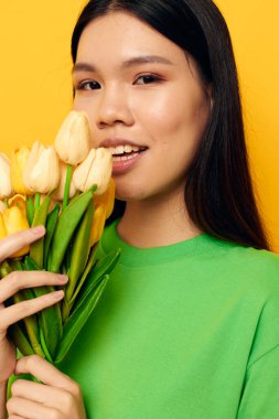 Çekici genç Asyalı kadın yeşil tişört bir buket sarı çiçek değiştirilmemiş arka plan