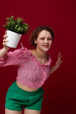 Çekici genç bir kadın ayakta duruyor ve saksıda çiçekleri tutuyor.