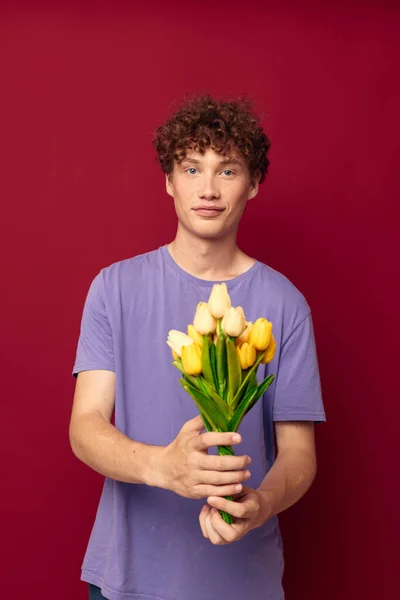 Söt tonåring som håller en gul bukett blommor lila t-shirts röd bakgrund oförändrad — Stockfoto