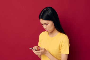 Asyalı bir kadın, sarı tişörtlü, elinde telefonla ortaya çıktı.