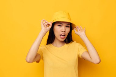 Sarı tişörtlü ve şapkalı çekici genç Asyalı kadın. Duygularını belli ediyor. Yaşam tarzı değişmemiş.