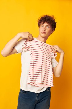 Beyaz tişörtlü, kırmızı kıvırcık saçlı adam çizgili tişört giyiyor. Gençlik tarzı, sarı arka plan değiştirilmemiş.