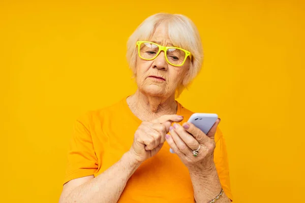 Mujer de edad avanzada en la comunicación casual camiseta por teléfono fondo amarillo — Foto de Stock