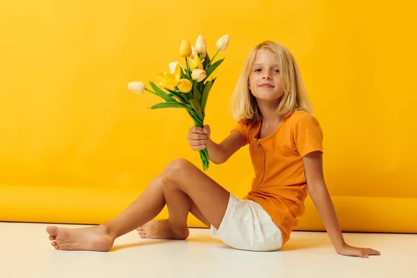 Kleines Mädchen sitzt auf dem Boden mit einem Strauß gelber Blumen Spaß gelben Hintergrund — Stockfoto