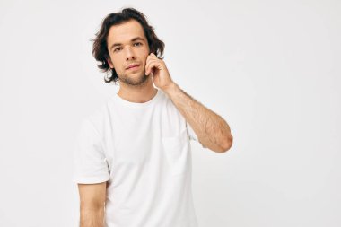 Beyaz tişörtlü bir adam. El hareketi. Arka plan hafif.