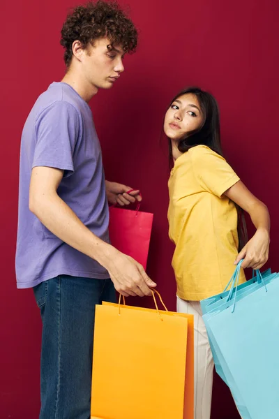 Portret van een man en een vrouw in kleurrijke T-shirts met tassen Winkelen geïsoleerde achtergrond ongewijzigd — Stockfoto