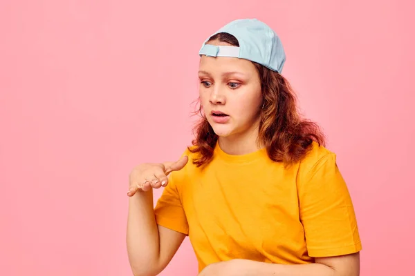 Bela mulher em uma camiseta amarela e azul cap posando emoções rosa fundo inalterado — Fotografia de Stock