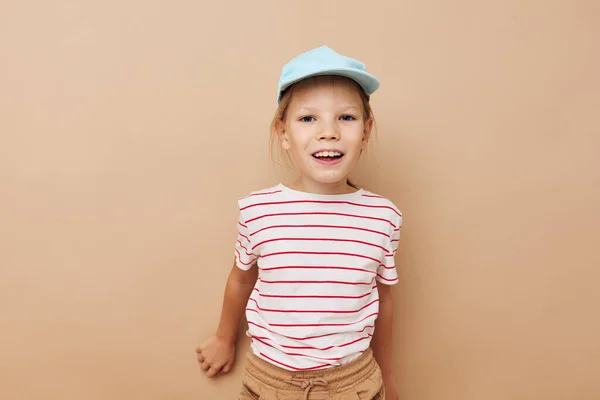 Mavi şapkalı, çizgili tişörtlü, bej arka planda mutlu gülümseyen kız çocuğu portresi — Stok fotoğraf