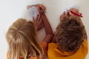 Neşeli çocuklar ellerinde not defterleri ve kalemlerle yere yatarlar. Çocukluk yaşam tarzları değişmez.