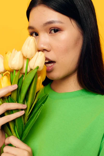 Woman with Asian appearance green t-shirt a bouquet of yellow flowers yellow background unaltered — Stockfoto