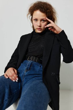 Siyah ceketli bir sandalyede oturan genç bir kadının portresi değiştirilmemiş arka planda poz veriyor.